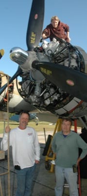 Mechanic Kaysha Raab performs a maintenance check on the B-17G as part of the scheduled yearly service for the Collings Foundation aircraft at American Aero Services. Company president Gary Norville (left) and Aero Services team member Vince Santorelly stand below.