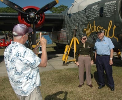 A visitor gets a photo of veterans Sam Mastrogiacomo and Joseph Reus (right) in front of the B-24 Liberator undergoing maintenance at American Aero.